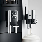 JURA Professional fine‑foam nozzle G2 (24250) connected to a coffee machine, chrome adapter and stream of milk foam into a container