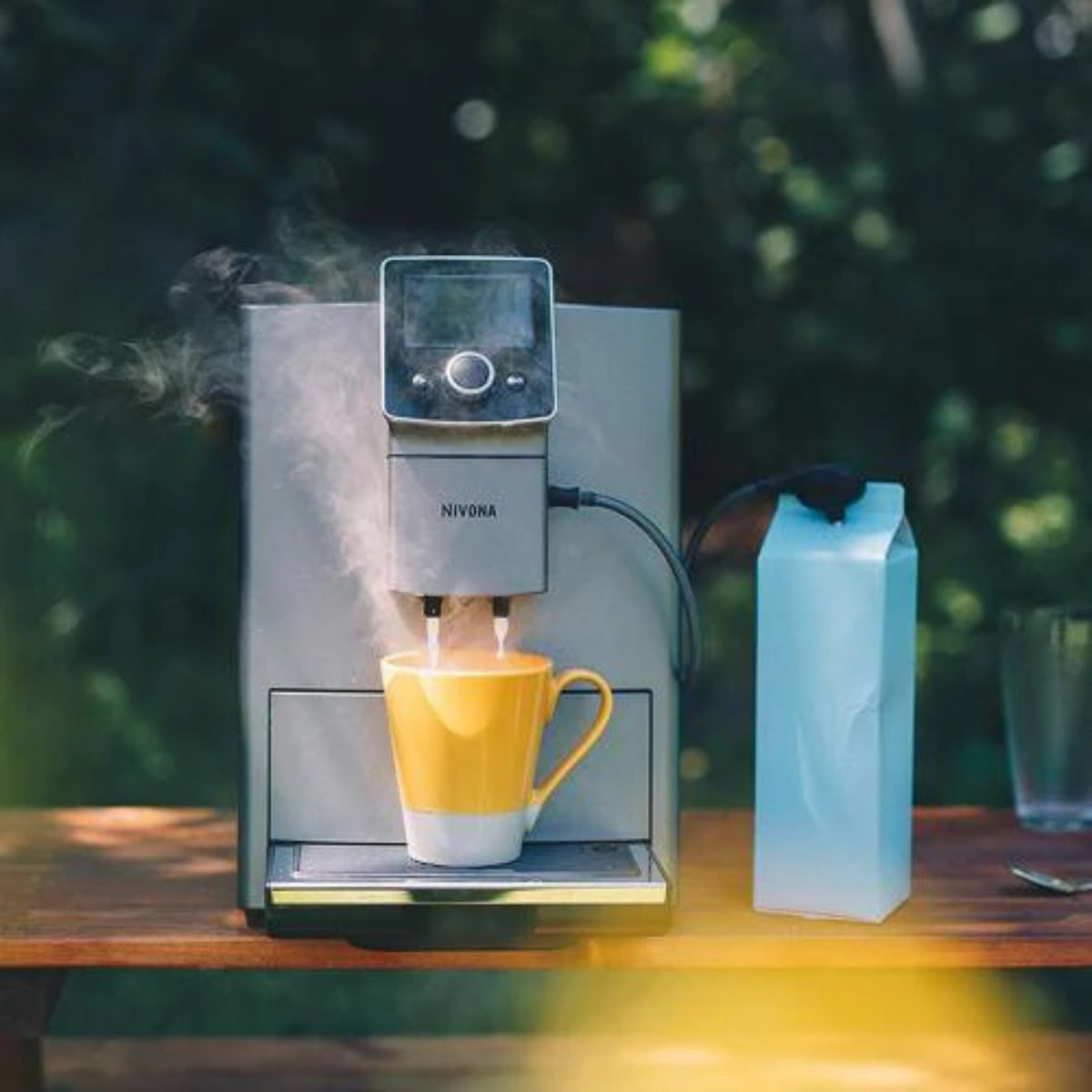 Nivona milk nozzle (NIML220) attached to coffee machine, silver nozzle with tube and steam issuing over a yellow cup
